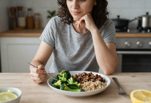 Person sitting at a kitchen table with a full meal in front of them while feeling hungry after eating and thinking about appetite signals