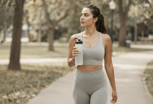 Woman walking outdoors in warm weather holding water bottle, showing common causes of early dehydration.