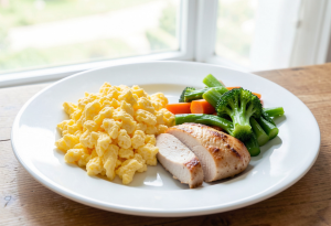 Plate with scrambled eggs, cooked chicken breast, and steamed vegetables for a high-protein meal.
