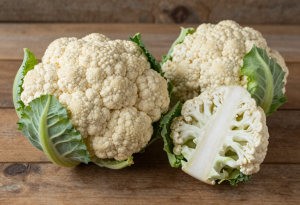 Fresh whole cauliflower on a wooden surface, showing white florets and green leaves for nutrition and digestive health
