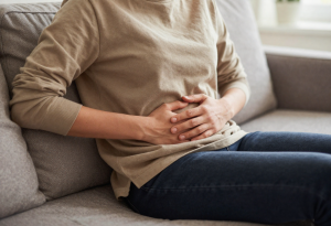 Person sitting on couch with hand on stomach looking uncomfortable, illustrating post-holiday bloating and gut reset