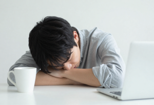 Tired person sitting at a desk with a coffee cup nearby, representing caffeine crash and low energy.