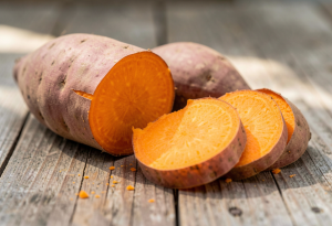 Baked sweet potato sliced open on a wooden surface, showing vibrant orange flesh for nutrition and energy support