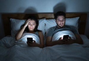 Person using a smartphone in bed at night, illustrating how late-night phone use can disrupt melatonin and cortisol balance.