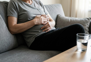 Person sitting with hand on abdomen while reading information about chronic bloating, representing common questions and answers