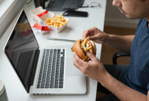 Person eating quickly at a desk while working, illustrating habits that may negatively affect digestion