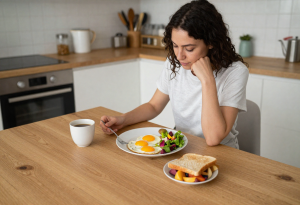 Woman eating a healthy breakfast at a kitchen table, illustrating why regular meals support metabolism