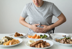 Person sitting at a table after eating a large meal, holding their stomach and looking uncomfortable