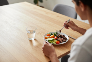 Wide-angle view of a person slowly eating a balanced meal at a sunlit dining table, illustrating the daily habit of mindful eating to support weight loss