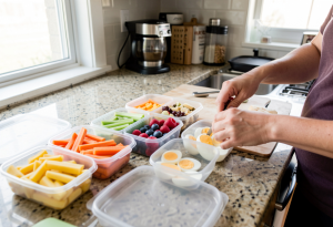Wide-angle view of prepped snack containers with fruits, vegetables, and boiled eggs on a kitchen counter, illustrating the habit of preparing healthy snacks to support weight loss