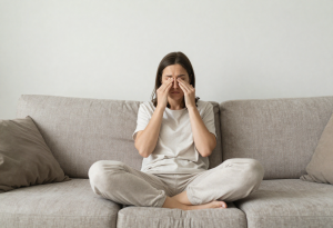 Woman in her early 30s sitting at home looking fatigued, noticing subtle body and weight changes during early perimenopause.