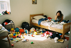 Stressed step-parent sitting on bed in messy kid’s room, overwhelmed by step-parenting responsibilities