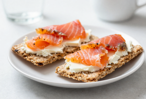 Two whole-grain crispbreads with smoked salmon and cream cheese on a plate, ready-to-eat snack