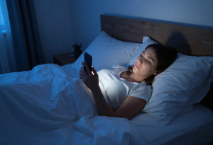 Attractive adult using smartphone in bed, illustrating blue light exposure and its effect on sleep tonight.