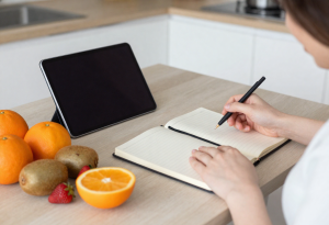 “Person reviewing a chart of vitamin C-rich foods with fruits like oranges, kiwis, and strawberries on the table”