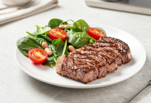 Plate with cooked steak and a salad containing spinach, beans, and cherry tomatoes, showing sources of dietary iron
