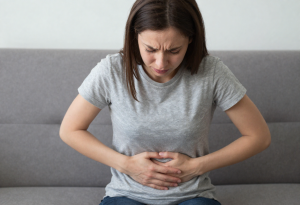 Woman sitting on a couch holding her stomach, illustrating mild digestive discomfort from excess iron intake