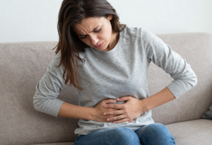 Woman sitting on a couch holding her stomach, illustrating potential digestive side effects of excessive vitamin C”