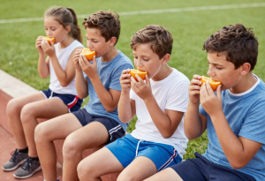 Children eating fresh oranges as a healthy snack at a sports field, rich in vitamin C