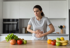Woman holding her stomach and looking concerned, surrounded by healthy foods, illustrating signs of an unhealthy gut