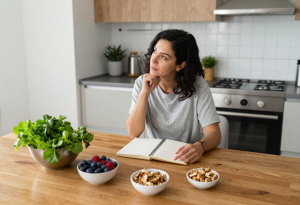 Woman sitting at a kitchen table with a notebook and liver-friendly foods like leafy greens, berries, and nuts, illustrating frequently asked questions about liver health