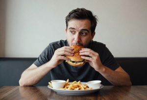 Person eating a burger and fries, illustrating cravings driven by hunger hormone imbalance
