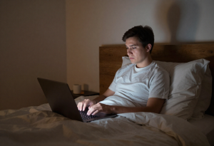 Person using a laptop in bed at night, illustrating how late-night screen use can disrupt sleep