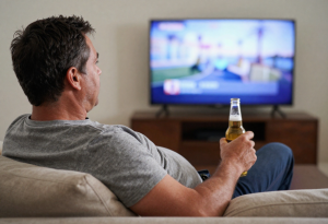 middle-aged man watching football at home drinking beer, showing lifestyle risk for liver health